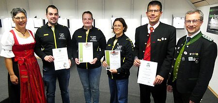 Sechs Personen stehen nebeneinander, vier halten Urkunden in den Händen, zwei tragen traditionelle Kleidung.